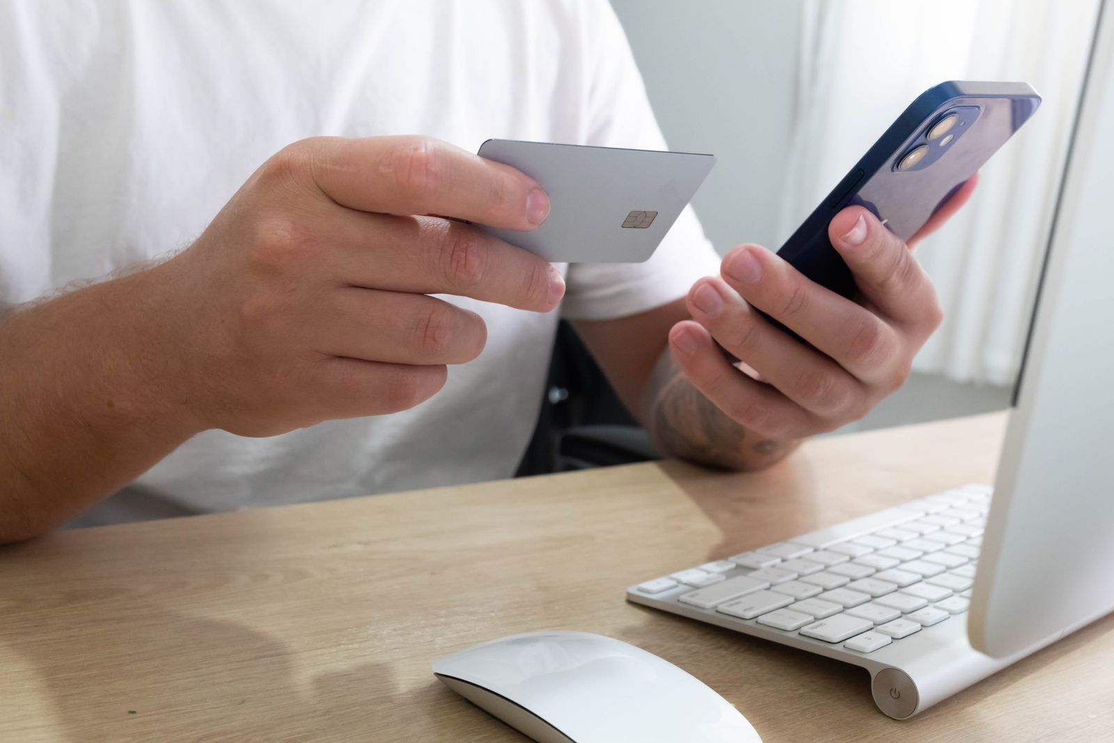 Hands holding a smartphone and bank card at a desk.