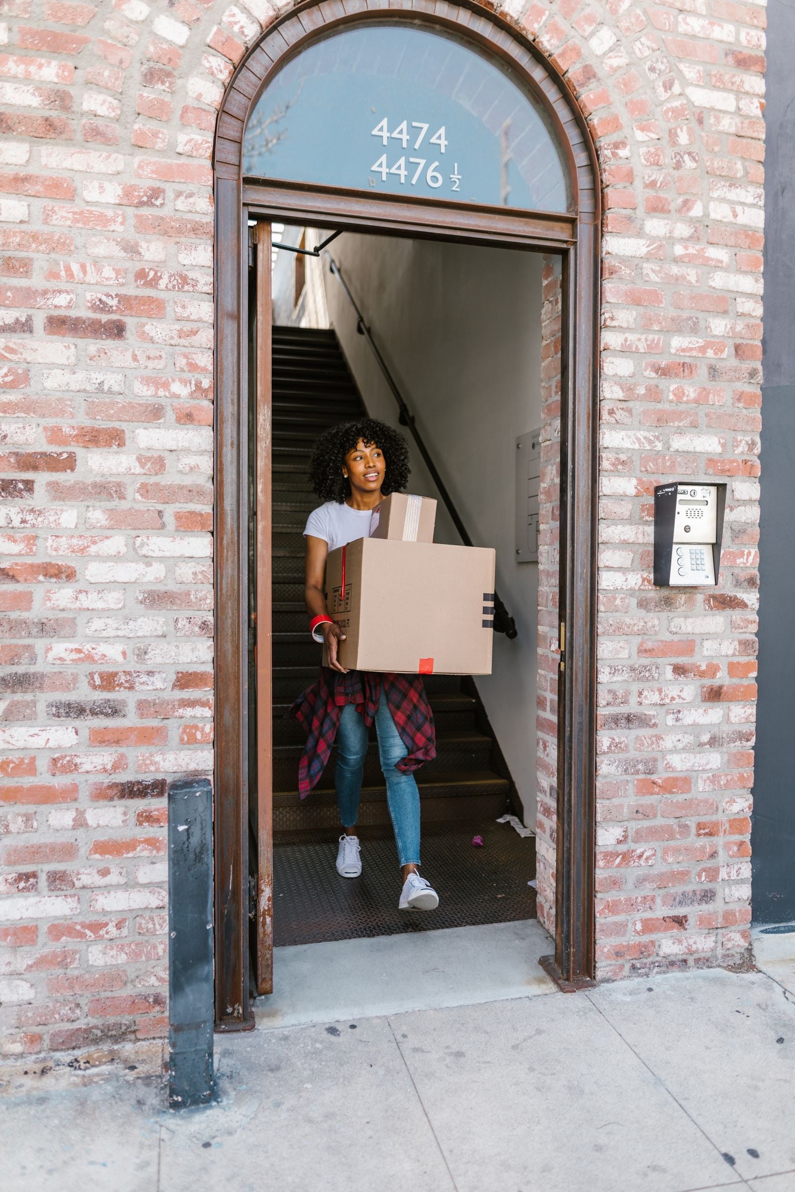 Woman carrying a cardboard box outside a brick building.